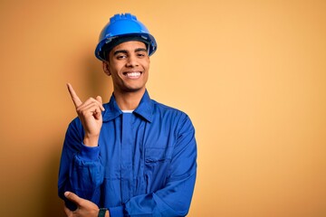 Young handsome african american worker man wearing blue uniform and security helmet with a big...