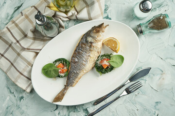 Appetizing baked sea bass with braised spinach salad on a white plate on a beige background. Top view, seafood