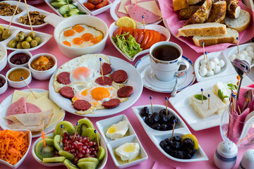 Traditional Turkish spreading breakfast with fry quail eggs and sausage egg on the middle of table with a cup of tea.Used completely white porcelain breakfast set.Pink ground and large view.