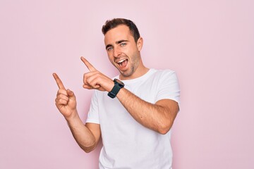 Handsome man with blue eyes wearing casual white t-shirt standing over pink background smiling and looking at the camera pointing with two hands and fingers to the side.