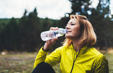 Girl quenches thirst after training fitness. Smile person drinking water from plastic bottles relax after exercising sport outdoors on nature, healthy lifestyle