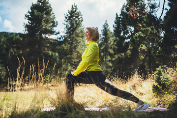 Fun girl one exercising outdoors in green forest sun summer day, activity with stretch legs. Smile fitness woman stretching exercises training outside. Sportswoman isolaition in nature