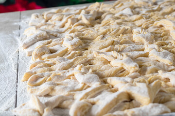 kitchen table. Sprinkled with flour. On it are dough products. Brushwood. Close-up