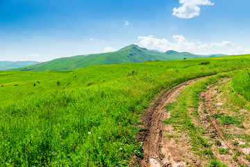 Dirty dirt road in a green field on a background of hills on a sunny day