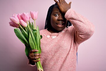 Young african american plus size woman with braids holding bouquet of pink tulips flower surprised...
