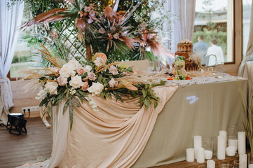 The table of the newlyweds, the presidium, with a gray linen tablecloth, a composition of flowers, on the background a lattice decorated with tropical leaves and branches of raspberries