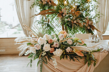 The table of the newlyweds, the presidium, with a gray linen tablecloth, a composition of flowers, on the background a lattice decorated with tropical leaves and branches of raspberries