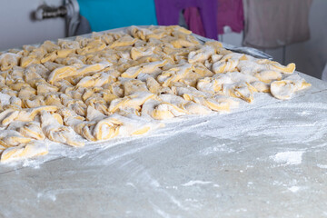 kitchen table. Sprinkled with flour. On it are dough products. Brushwood. Close-up