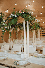 Restaurant, served table, rustic, huge compositions of flowers and tropical leaves on the table, plates, cutlery, crystal glasses, wooden chairs, garlands of light bulbs.