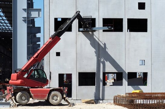 A telescopic handler, from exterior, brings up some steel bars to the first floor of the building under construction