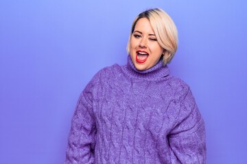 Beautiful blonde plus size woman wearing casual turtleneck sweater over purple background winking looking at the camera with sexy expression, cheerful and happy face.