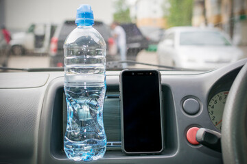Smartphone and a bottle of mineral water on the car panel.