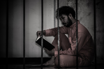Fototapeta na wymiar Asian man desperate at the iron prison,prisoner concept,thailand people,Hope to be free,Serious prisoners imprisoned in the prison,Reading a book