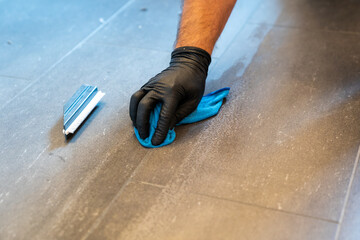 close up of professional cleaner cleaning grout with a blue cloth rag and foamy soap on a gray tiled bathroom floor