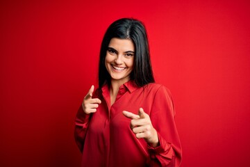 Young beautiful brunette woman wearing casual shirt standing over red background pointing fingers to camera with happy and funny face. Good energy and vibes.
