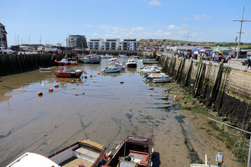 A view of the pretty harbour at West Bay with Pleasure boats and fishing boats at moorings with low tide in a sunny day. Dorset, UK