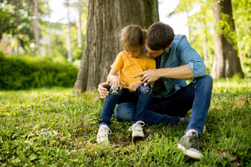 Single father sitting on grass by the tree with little daughter