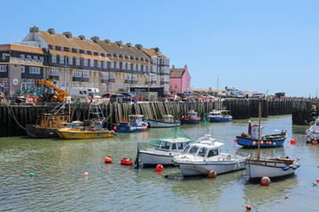 A view of the pretty harbour at West Bay with Pleasure boats and fishing boats at moorings with low tide in a sunny day. Dorset, UK