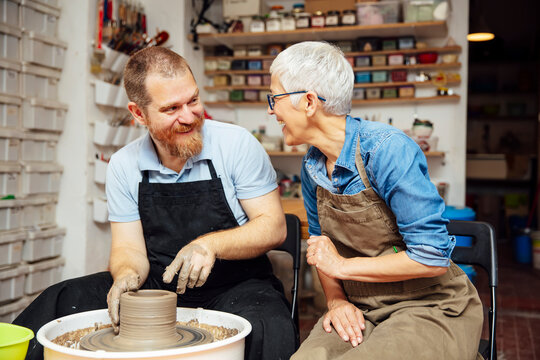 Senior woman spinning clay on a wheel with teacher at pottery class