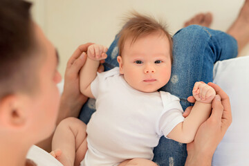 Father and baby son play on a white bed in a sunny bedroom. Parent and little child are resting at home. Family having fun together.
