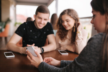 Group of tree friends on terrace. Yound people meeting in cafe. Friends sitting in cafe together. Female show to couple something on her smartphone