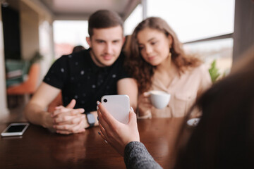 Group of tree friends on terrace. Yound people meeting in cafe. Friends sitting in cafe together. Female show to couple something on her smartphone