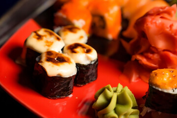 Hot gunkan sushi with cheese on the red dish with wasabi. Assorti of sushi philadelphia maki. 