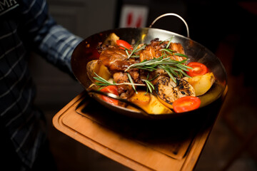 Roasted meat in a pan with potato and tomatoes, seasoned rosemary leaves.