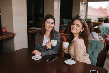 Two female friends drink coffe in restauratn and speak. Beautiful women metting in cafe. End of quarantine