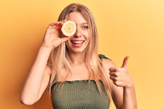 Young blonde woman holding lemon smiling happy and positive, thumb up doing excellent and approval sign