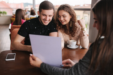 Happy couple in cafe meet with bussines woman. Woman show to man and woman something on documents