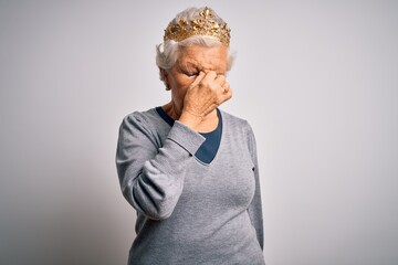 Senior beautiful grey-haired woman wearing golden queen crown over white background tired rubbing nose and eyes feeling fatigue and headache. Stress and frustration concept.