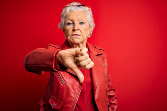 Senior beautiful grey-haired woman wearing casual red jacket and sunglasses looking unhappy and angry showing rejection and negative with thumbs down gesture. Bad expression.