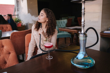 Attractive young woman smoke hookah in restaurant. Woman with hookah on terrace by herself