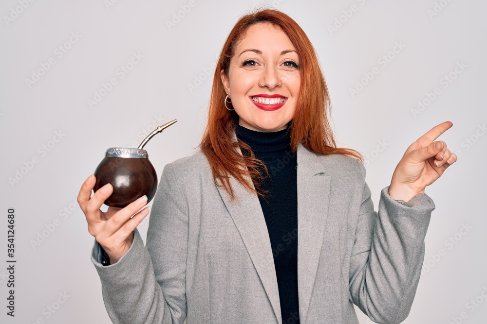 Poster young beautiful redhead woman drinking argentina mate beverage over white background very happy poin