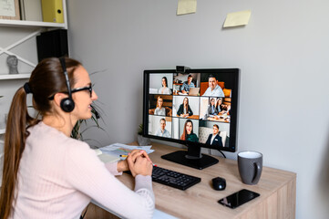 A young female superior is listening to reports of her subordinates using a video app on PC, a back...