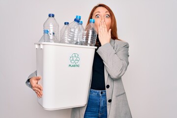 Young beautiful redhead woman recycling holding trash can with plastic bottles to recycle cover mouth with hand shocked with shame for mistake, expression of fear, scared in silence, secret concept