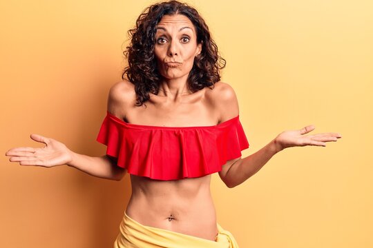 Middle age beautiful woman wearing bikini clueless and confused with open arms, no idea and doubtful face.