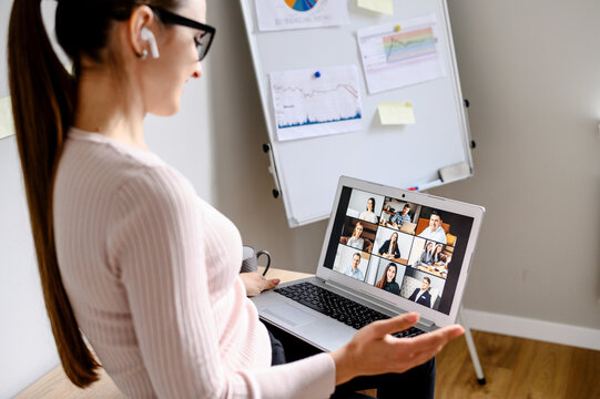 Online video discussion with many people together. Young woman sits in front of laptop with many icons, photo profiles of people on screen. App for video meeting, office with flip chart