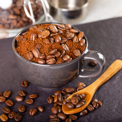 Ground coffee in a black cup, and at the top several roasted coffee beans.