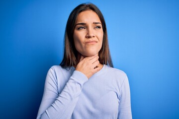 Obraz premium Young beautiful brunette woman wearing casual sweater standing over blue background Touching painful neck, sore throat for flu, clod and infection