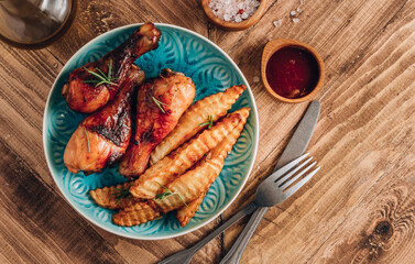 Chicken drumsticks with french fries on blue plate on rustic wooden table.