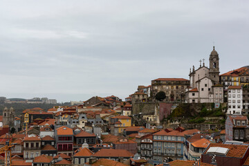 Fototapeta na wymiar View to Porto's downtown (Portugal) from the cathedral view point. Church on the top of the hill. Portuguese traditional houses with orange roofs.