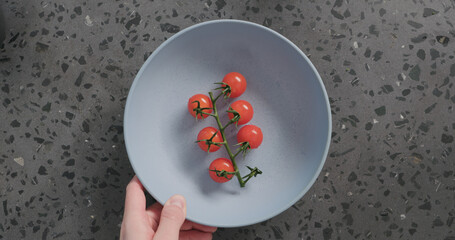 Top view man hand put cherry tomatoes in blue ceramic bowl on concrete background