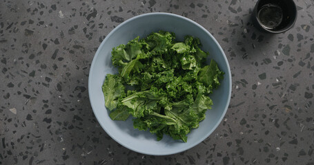 Top view massaged kale leaves in blue ceramic bowl on concrete background