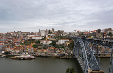 Fototapeta na wymiar Porto (Portugal) view, with Dom Luís Bridge and metro. Sunset, cloudy sky. Boats on the river.