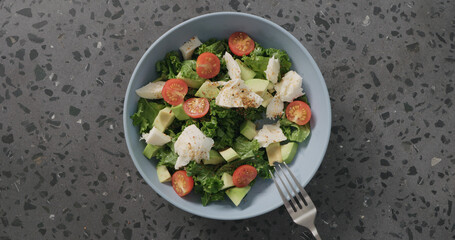 Top view salad with tomatoes , avocado, mozzarella and kale leaves in blue ceramic bowl on concrete background