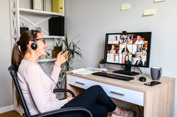 Obraz na płótnie Canvas Young successful employee is have a meeting with her team using a headset, she is sitting relaxed and smiling, a middle side shot.