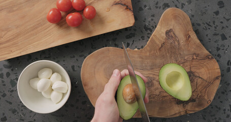 Top view man hands cut in halves and open ripe avocado on concrete countertop
