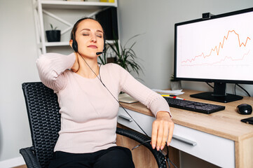 Tired from work young woman with a headset at the office desk, she is holding her head with a eyes...
